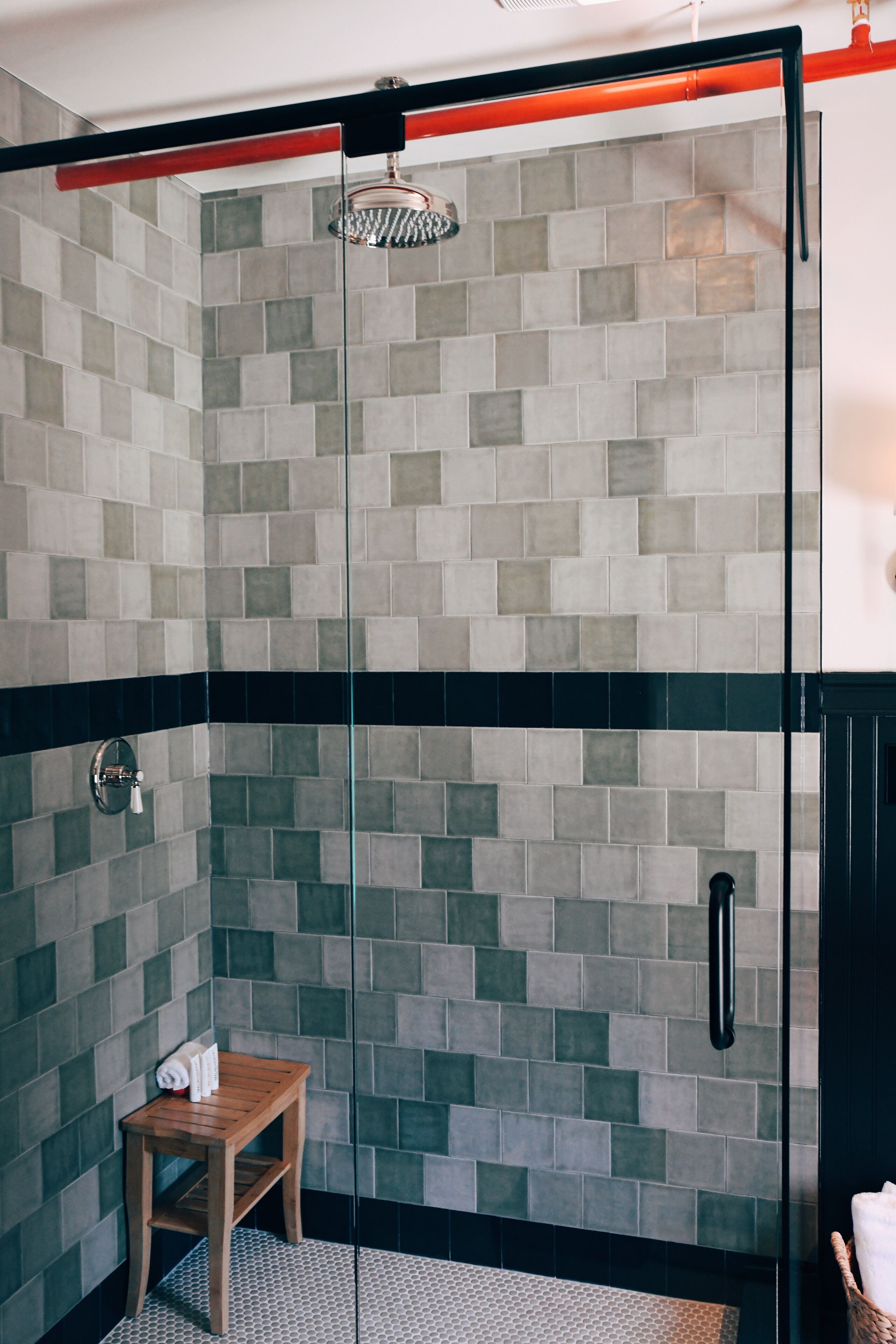 A shower with a glass door, tiled walls, and a wooden stool.