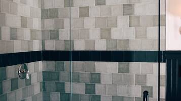 A shower with a glass door, tiled walls, and a wooden stool.