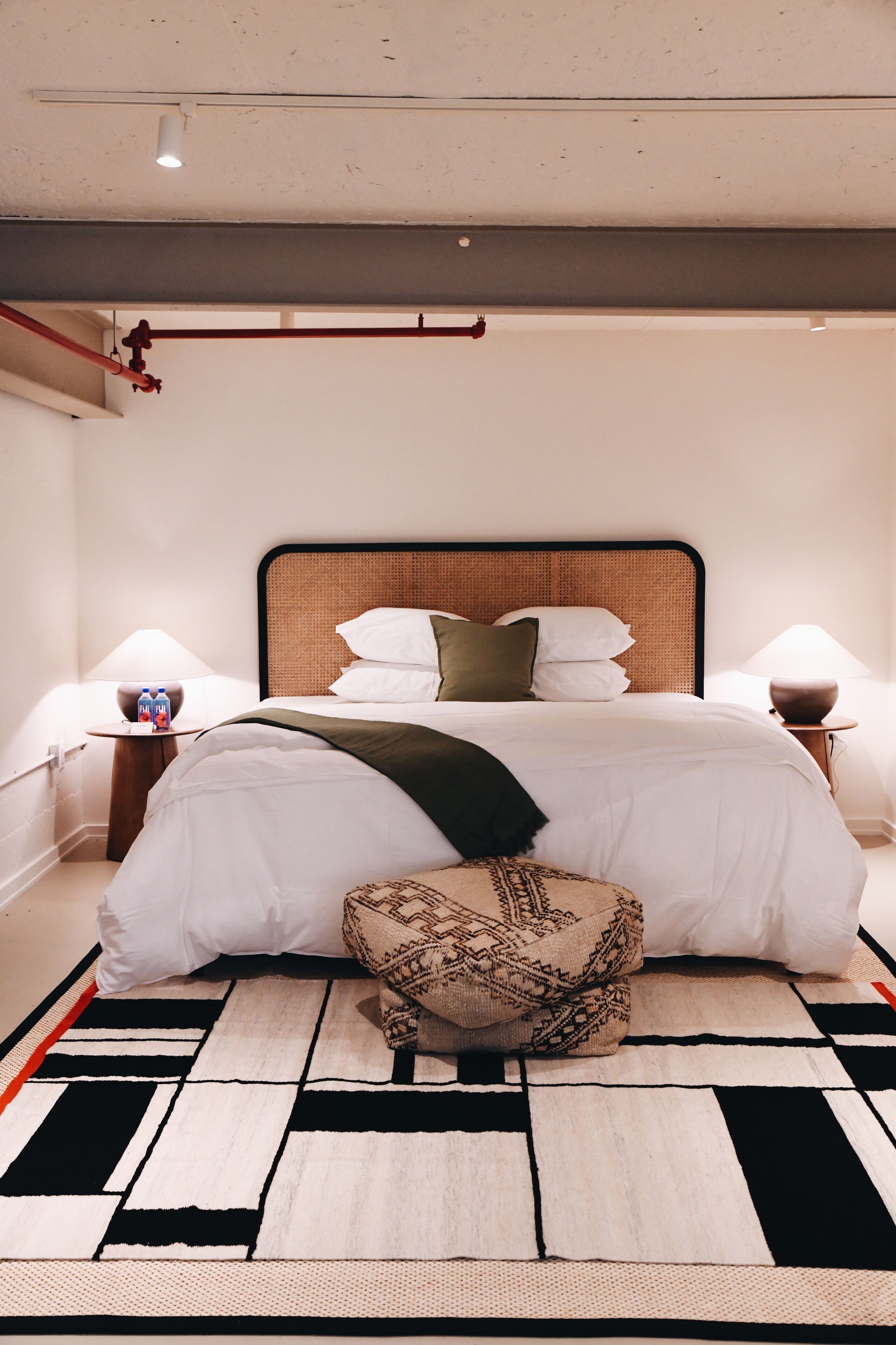 A modern hotel room with a large bed, a bedside table with a lamp, and a decorative pillow.