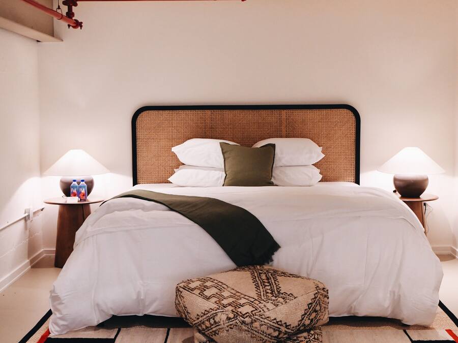 A modern hotel room with a large bed, a bedside table with a lamp, and a decorative pillow.