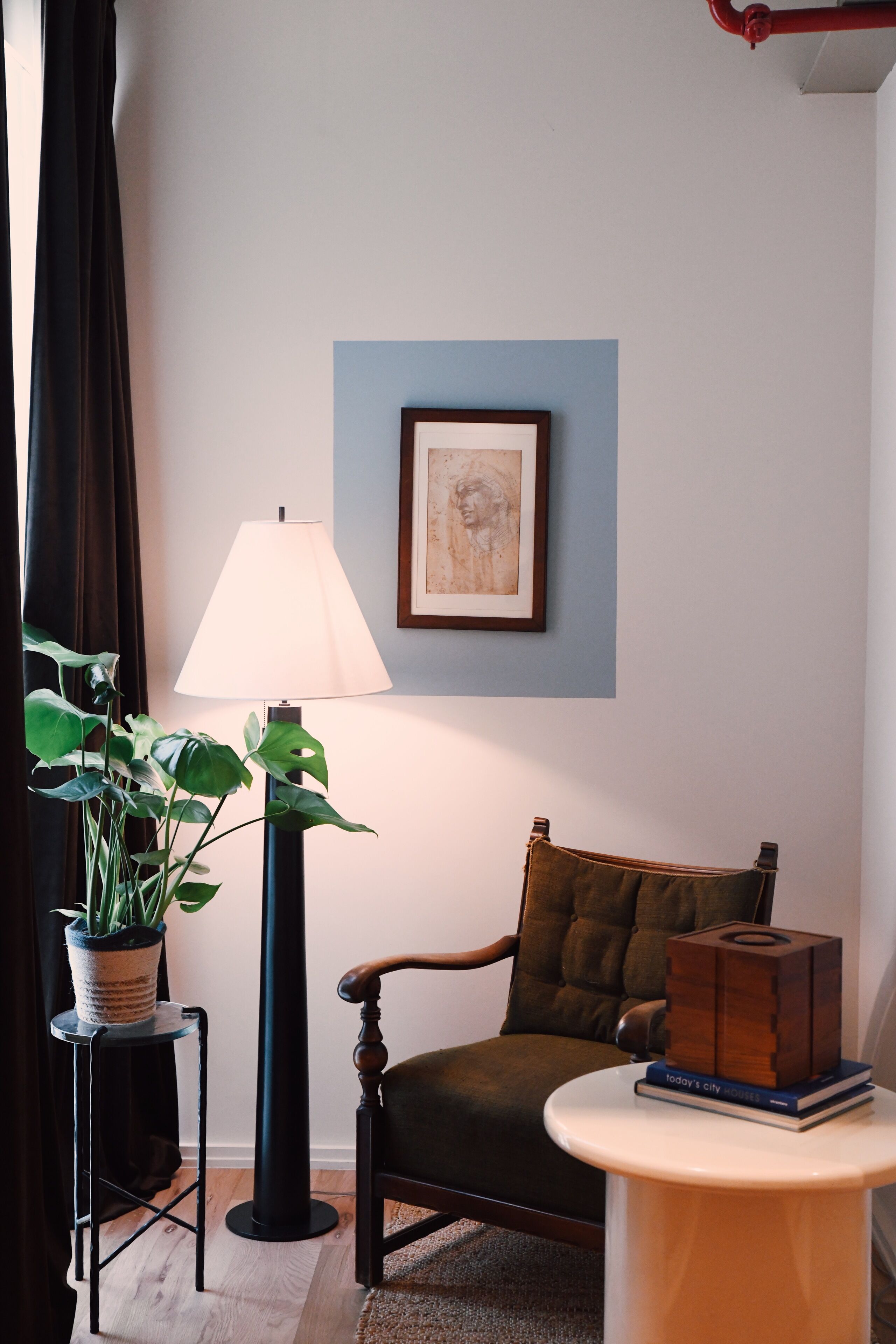 Quarto com cadeira, luminária, mesa, quadro emoldurado e planta em vaso.