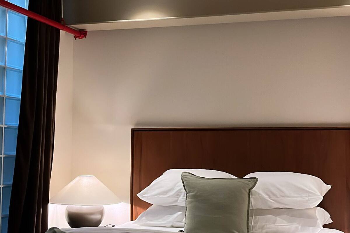A hotel room with a bed, a nightstand, a lamp, and a window with curtains.