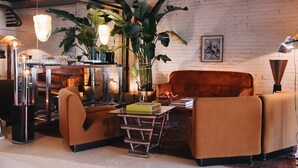 A modern living room with a brick wall, a brown leather sofa, a glass coffee table, and a large plant.