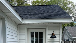 A white house with a black roof, a front door with a window, a black doormat, and a blue potted plant. - Charming Lake Huron cottage (Tawas City)