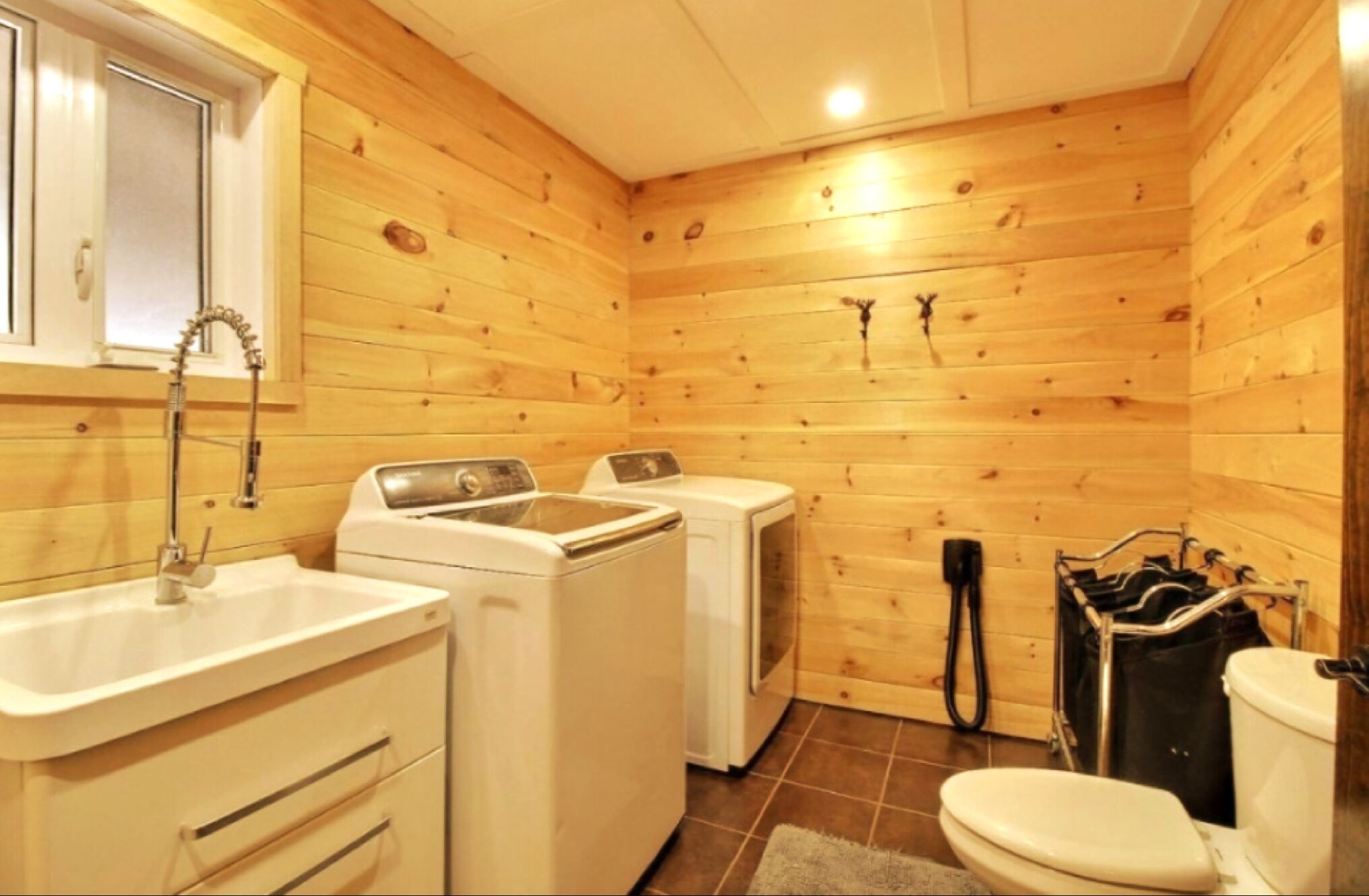 Une petite salle de bain en bois, aménagée dans une cabane, et comprenant une machine à laver, un lavabo et des toilettes.