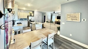 A modern kitchen with white cabinets, a stainless steel refrigerator, and a dining area with a wooden table and chairs. - NEW Putt Chip&Chill 3BRTownhouse NMB SportsComplex (little river)