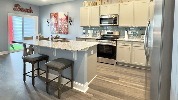 A modern kitchen with a central island, stainless steel appliances, and a 'WELCOME' sign above the cabinets. - NEW Putt Chip&Chill 3BRTownhouse NMB SportsComplex (little river)