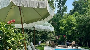 Un área junto a la piscina con sillones de descanso y una sombrilla grande.