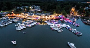 A marina with numerous boats docked, a large illuminated building with a sign, and a docked boat with a person on it.