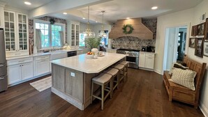 Una cocina amplia con una isla grande, armarios de madera, una pared de acento de piedra y una estufa empotrada.