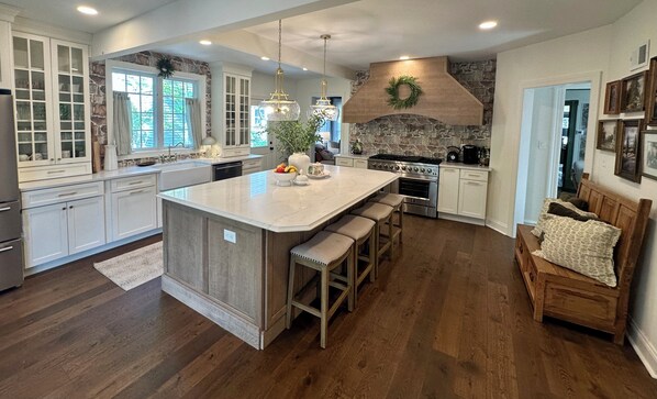 A spacious kitchen with a large island, wooden cabinets, a stone accent wall, and a built-in stove.