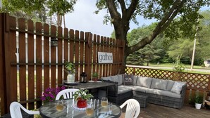 A wooden deck with a glass table, white chairs, a sofa, and potted plants. - Rapid River Retreat! Home sleeps 6, garage, fire pit (Rapid City)