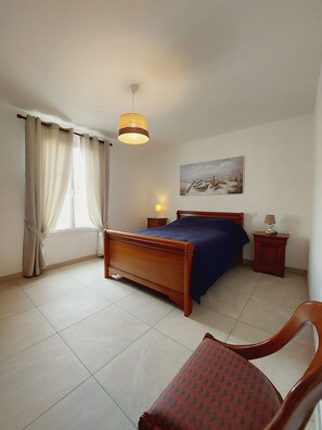A bedroom with a wooden bed, a chair, a nightstand, a lamp, a painting on the wall, and a window with curtains. - Regarding a WITHDRAWN LISTING: BEAUTIFUL 3-STAR-RATED HOUSE IN LA COTINIERE (Saint-Pierre D Oleron)