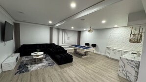 Una sala de estar moderna con mesa de billar, sofá seccional negro y alfombra con diseño de mármol.