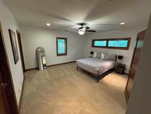 A bedroom with a bed, a ceiling fan, a window, and a door.