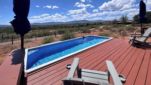 Ein Schwimmbecken auf einer Holzterrasse mit zwei Liegestühlen und einem Sonnenschirm, umgeben von einer Wüstenlandschaft.