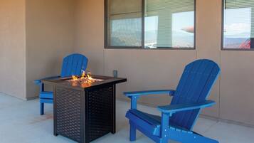 Un espace patio aménagé avec une table en métal noir, deux fauteuils Adirondack bleus et un petit foyer extérieur.