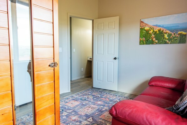 A room with a red leather sofa, a patterned rug, and a white door leading to a hallway.