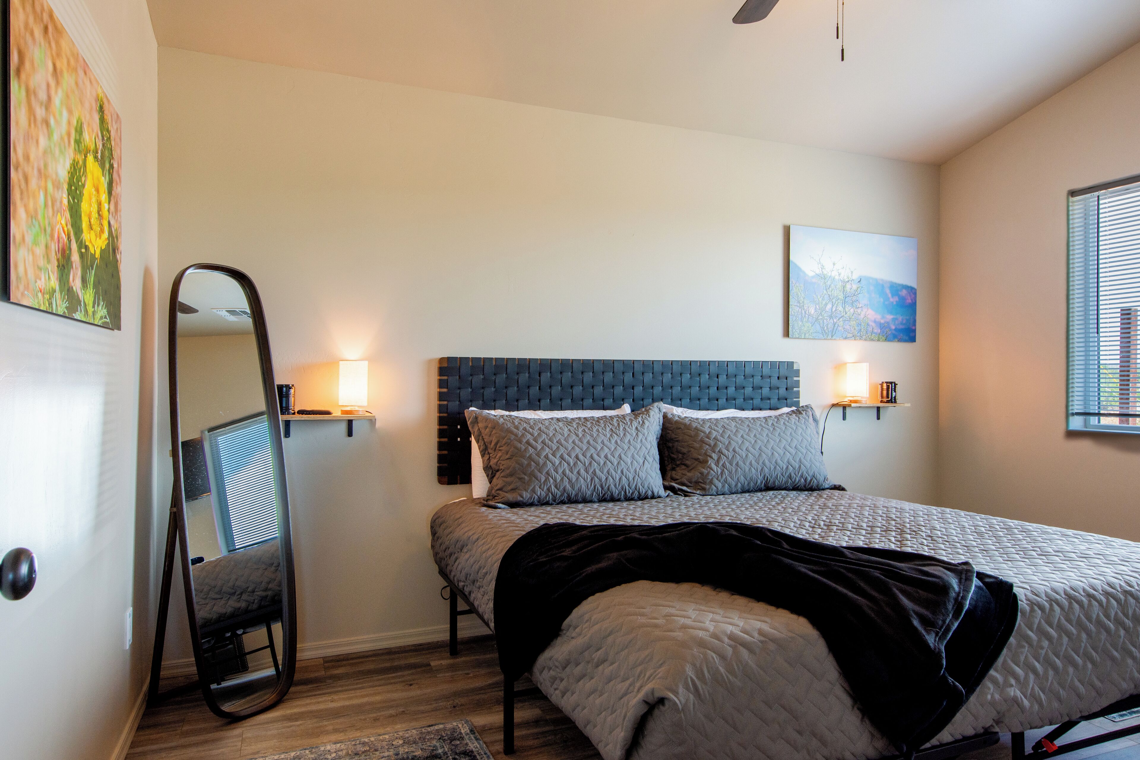 A bedroom with a bed, bedside lamps, a mirror, and artwork on the walls.