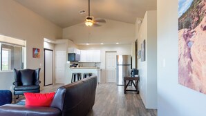 A modern living room with a black leather sofa, a red pillow, and a black armchair. There is a kitchen area with white cabinets and a refrigerator in the background. - Private Wine Country Retreat • 2 Suites & 2 Hot Tubs (Cornville)