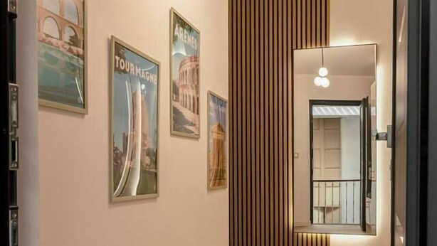 A hallway with wooden flooring, framed travel posters on the walls, and a modern light fixture. - ✨ L'Instant Nîmois - Natural elegance in the heart of Nîmes ✨ (Nîmes)