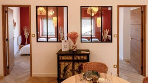 A hotel room with a dining area, a large mirror, and a view of the adjacent room. - ✨ L'Instant Nîmois - Natural elegance in the heart of Nîmes ✨ (Nîmes)