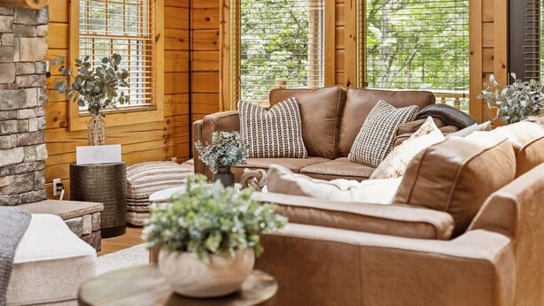 A cozy living room with a brown leather sofa, patterned cushions, a woven side table, and a potted plant. - Trails End- Sauna, Hot Tub, Fire pit, Arcade, King Beds, Luxury stay, less than 8 miles to all attractions/hikes (Logan)