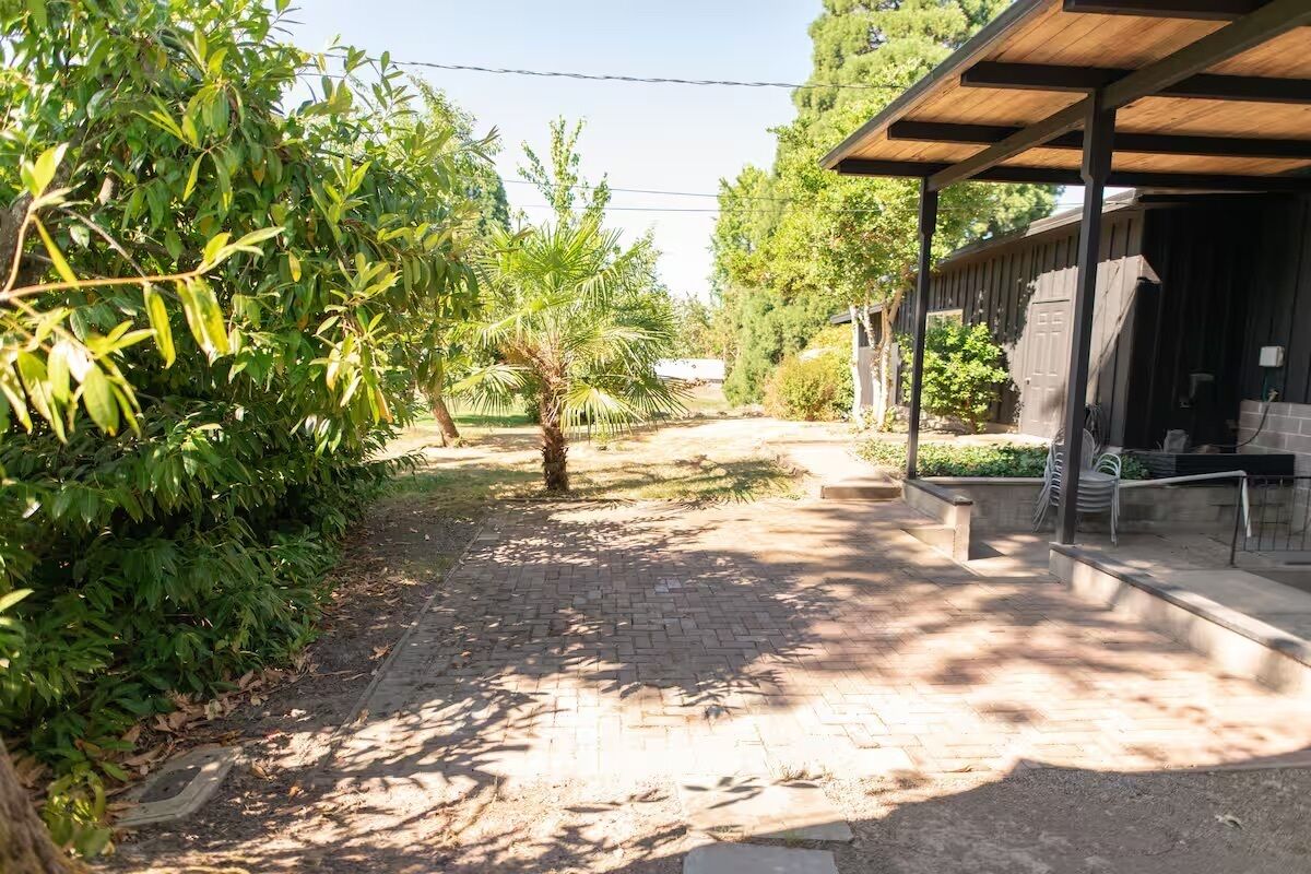 A paved pathway leading to a covered outdoor area with a building on the right.