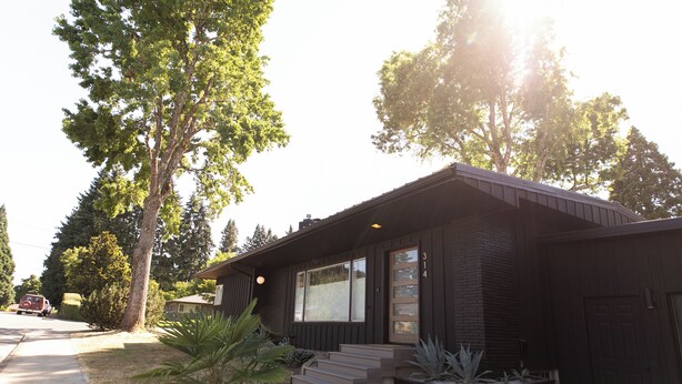 Une maison moderne à deux étages, avec une façade sombre, un porche à l’avant et un garage.