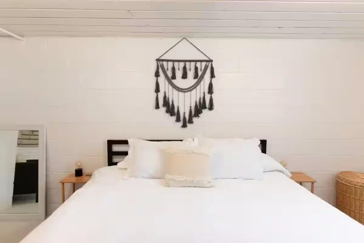 Een net opgemaakt bed met witte lakens en een decoratieve wandhanger erboven.