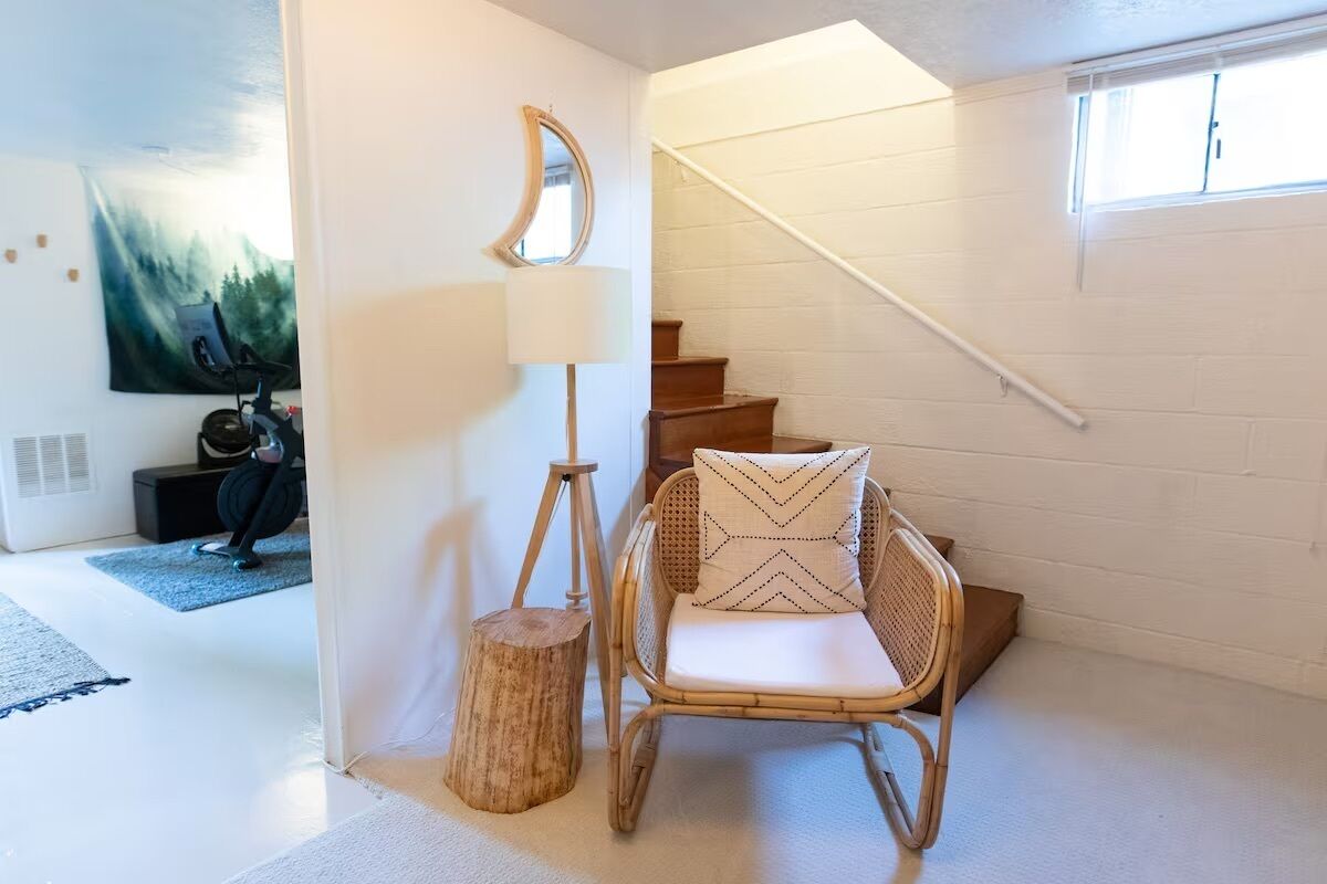 Una habitación con una silla de mimbre, una lámpara y un cuadro en la pared.