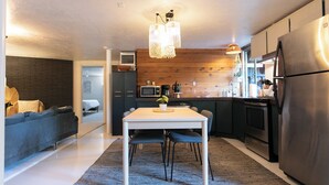 Une cuisine moderne avec un coin repas, comprenant une table blanche, des chaises foncées et un luminaire suspendu.