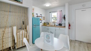 Cocina compacta con refrigerador color turquesa, gabinetes blancos, microondas y un ventanal con cortina.