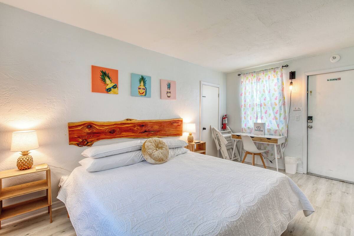 A bedroom with a wooden headboard, a bed with white bedding, a desk with a chair, and a "No Smoking" sign on the door.