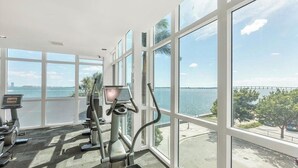 A gym with cardio machines and a large window overlooking a body of water and a bridge. - Modern 2BR Apartment in Brickell, Central w Sea View (Miami)