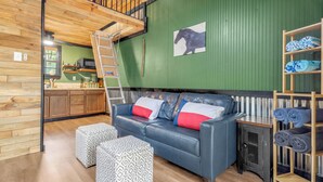 A cozy room with a blue leather sofa, patterned ottomans, a wooden ladder, and a green wall with a horse painting.
