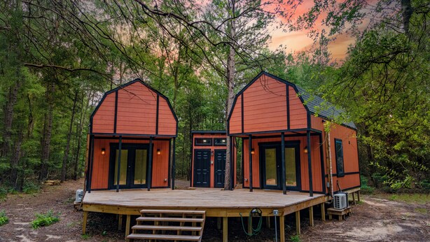 Eine Holzhütte mit einer Holzterrasse und zwei daran angebauten Gebäuden, umgeben von Bäumen.