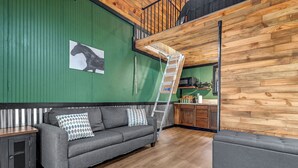 Ein modernes Wohnzimmer mit grauem Sofa, einer Bank, einer Leiter und einer Holzwand mit einem Pferdebild.