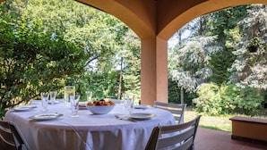 An outdoor dining area with a round table set for two, surrounded by chairs, with a view of trees and greenery. - Villa La Fortezza - Six Bedroom Villa, Sleeps 12 (Dormelletto)