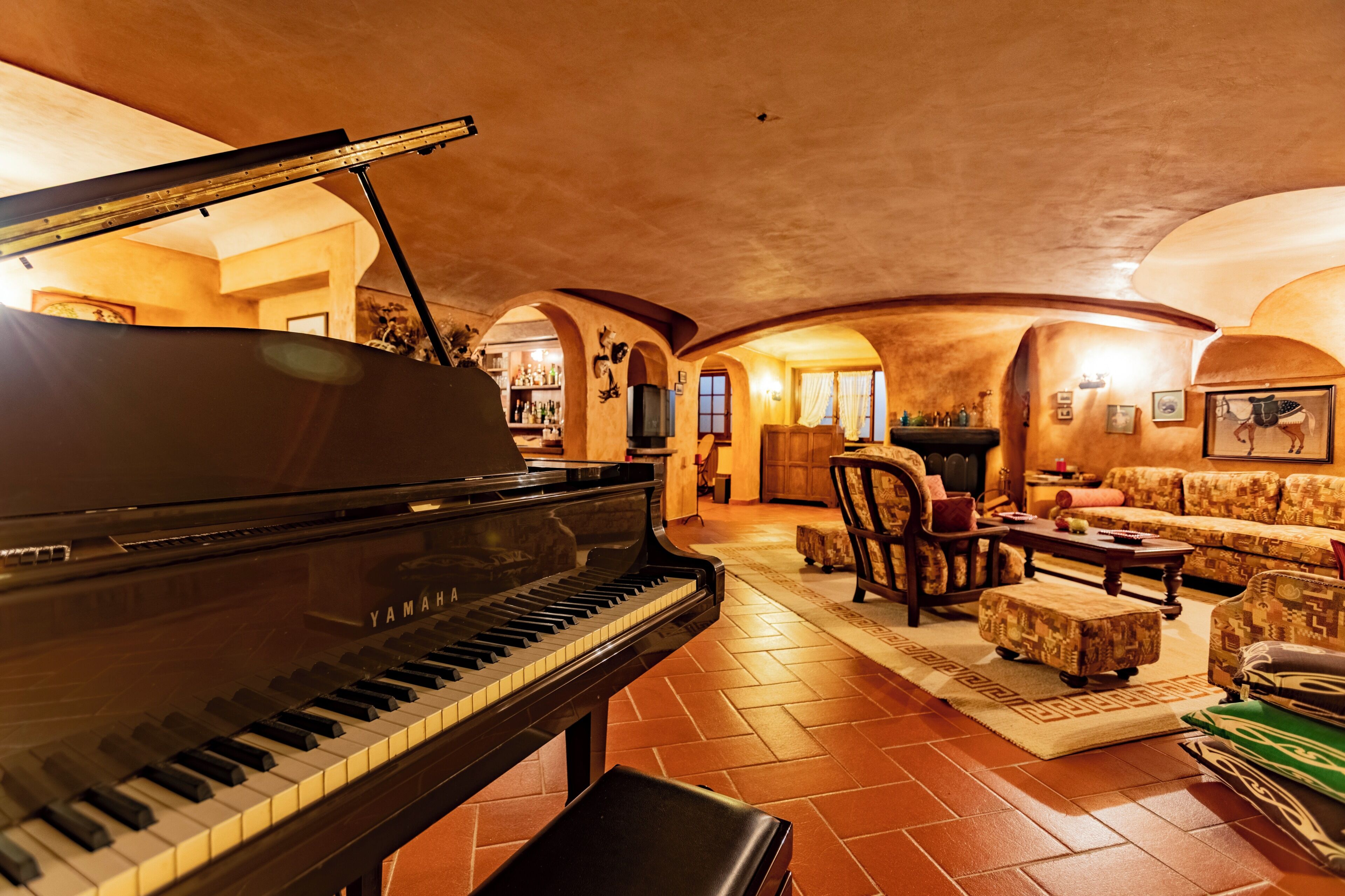 Un piano à queue dans une pièce chaleureuse, éclairée d’une lumière douce, avec une cheminée, des fauteuils confortables et un sol carrelé.