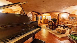 A grand piano in a warmly lit room with a fireplace, comfortable seating, and a tiled floor. - Villa La Fortezza - Six Bedroom Villa, Sleeps 12 (Dormelletto)