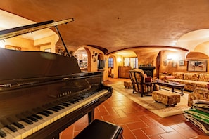 Een vleugelpiano in een warm verlichte kamer met een open haard, zachte zitplaatsen en een betegelde vloer.