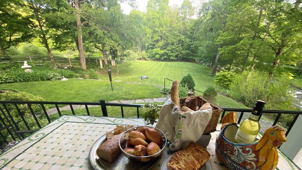 A table with various food items and a bottle of wine, overlooking a lush garden. - Private bedroom in the Green River Bridge Inn. A full breakfast is included. (Guilford)