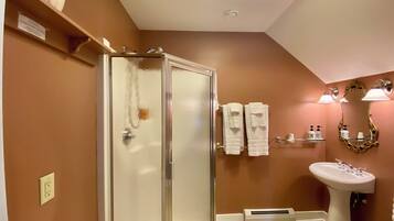 A bathroom with a glass shower door, a pedestal sink, and a vanity mirror.