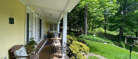 A porch with a table set for two, a chair, and a potted plant.