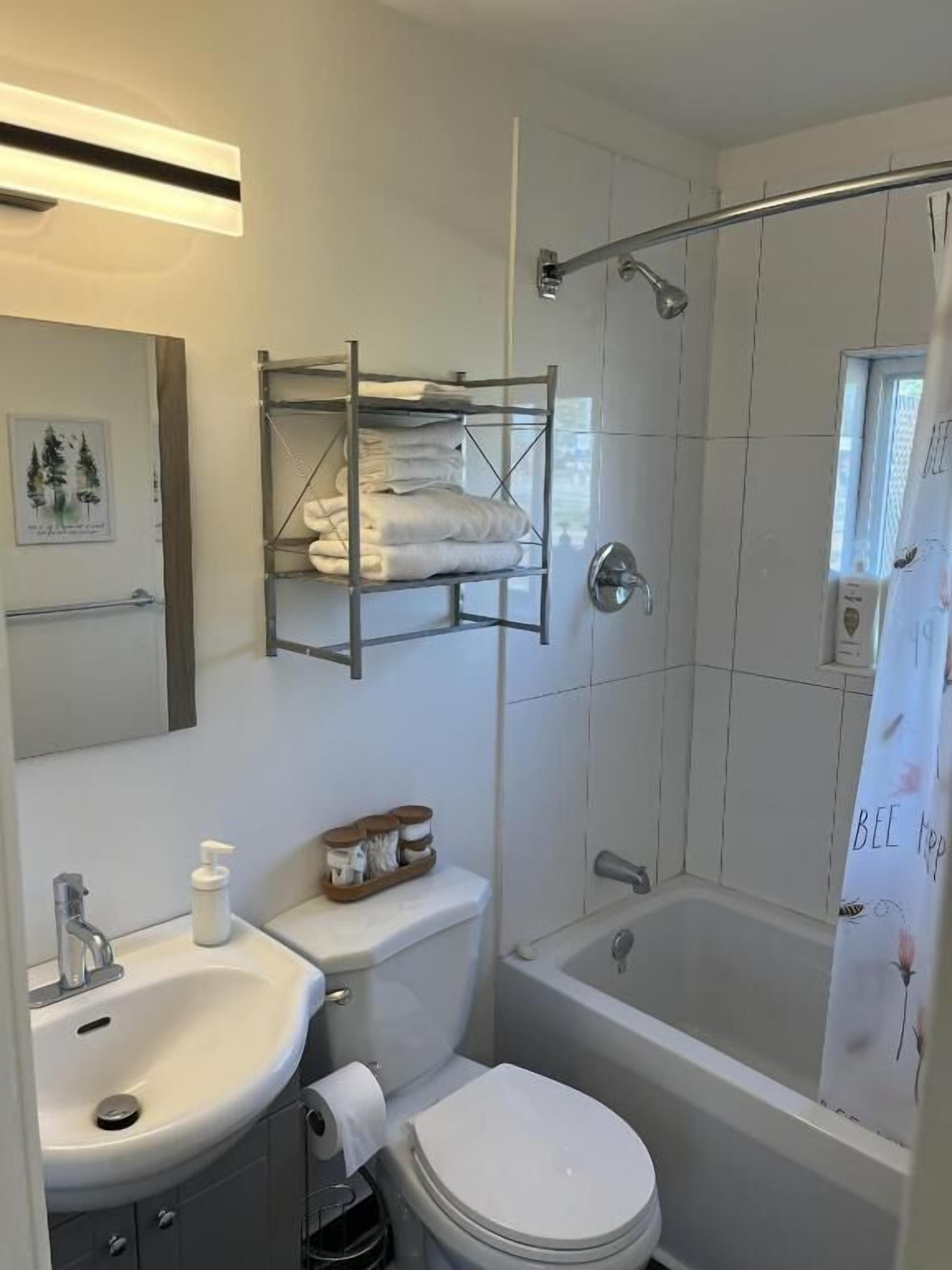 Une salle de bain avec un lavabo, des toilettes et une baignoire. On y trouve une étagère avec des serviettes et un rideau de douche à motifs floraux.