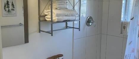 Un baño con lavamanos, inodoro y bañera. Hay un estante con toallas y una cortina de ducha con diseño floral.