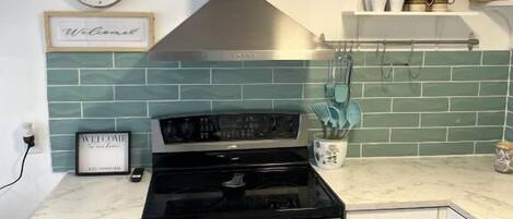 A kitchen with a stainless steel stove, white cabinets, a green tiled backsplash, and a clock on the wall.