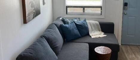 A modern living room with a gray sectional sofa, a small round coffee table, and a window with blinds.