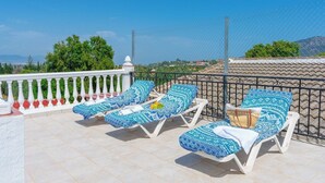 A terrace with four sun loungers, a white balustrade, and a view of the landscape.